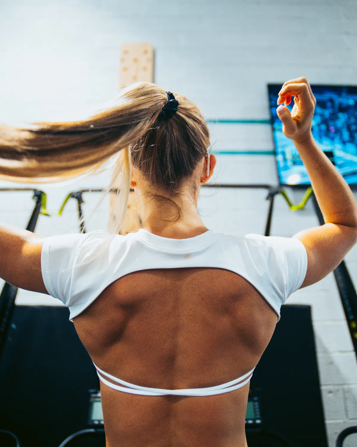The coach raises her arms in a gym, seen from behind.